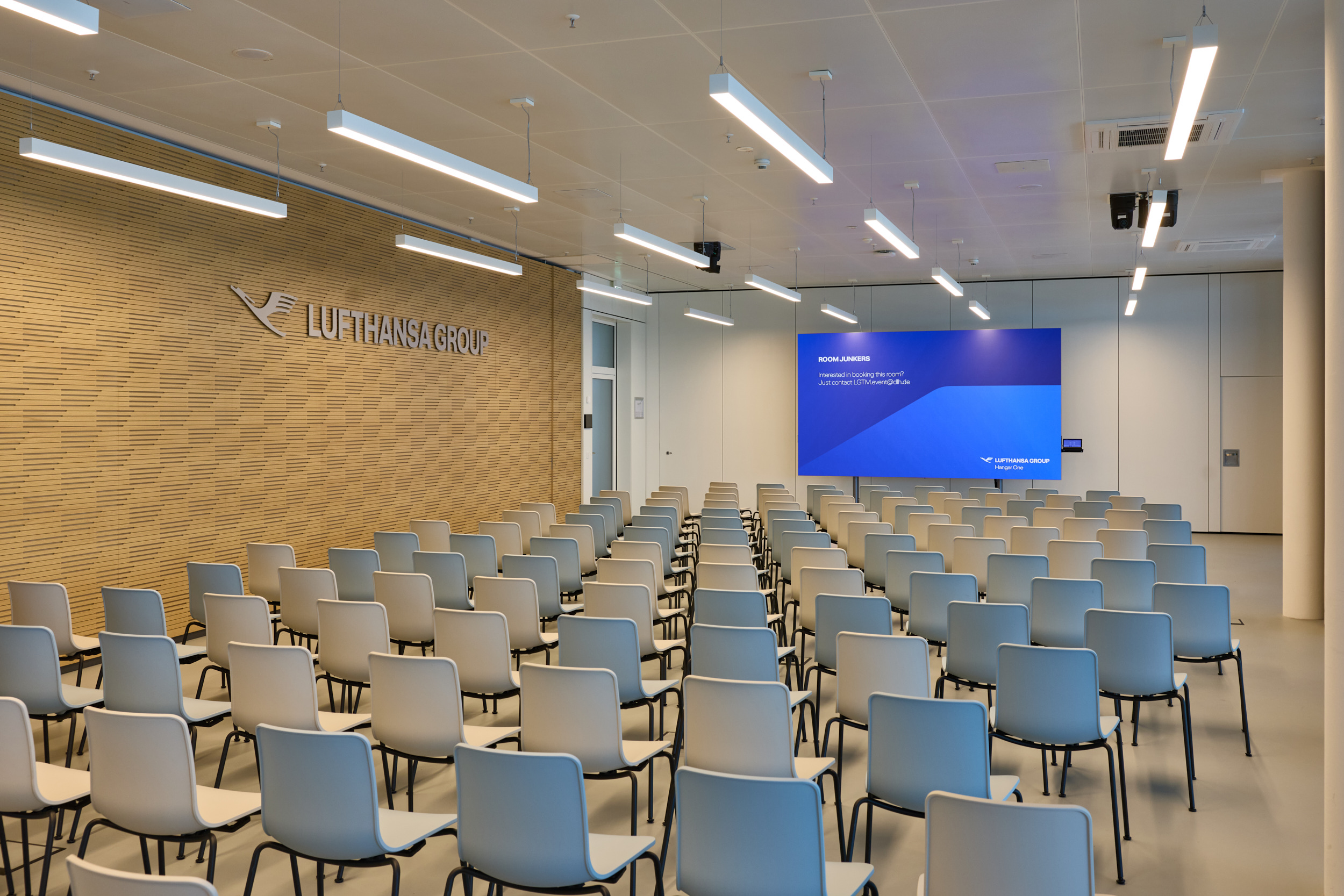 Large event room with U-shaped tables, microphones, screens, and a presentation area